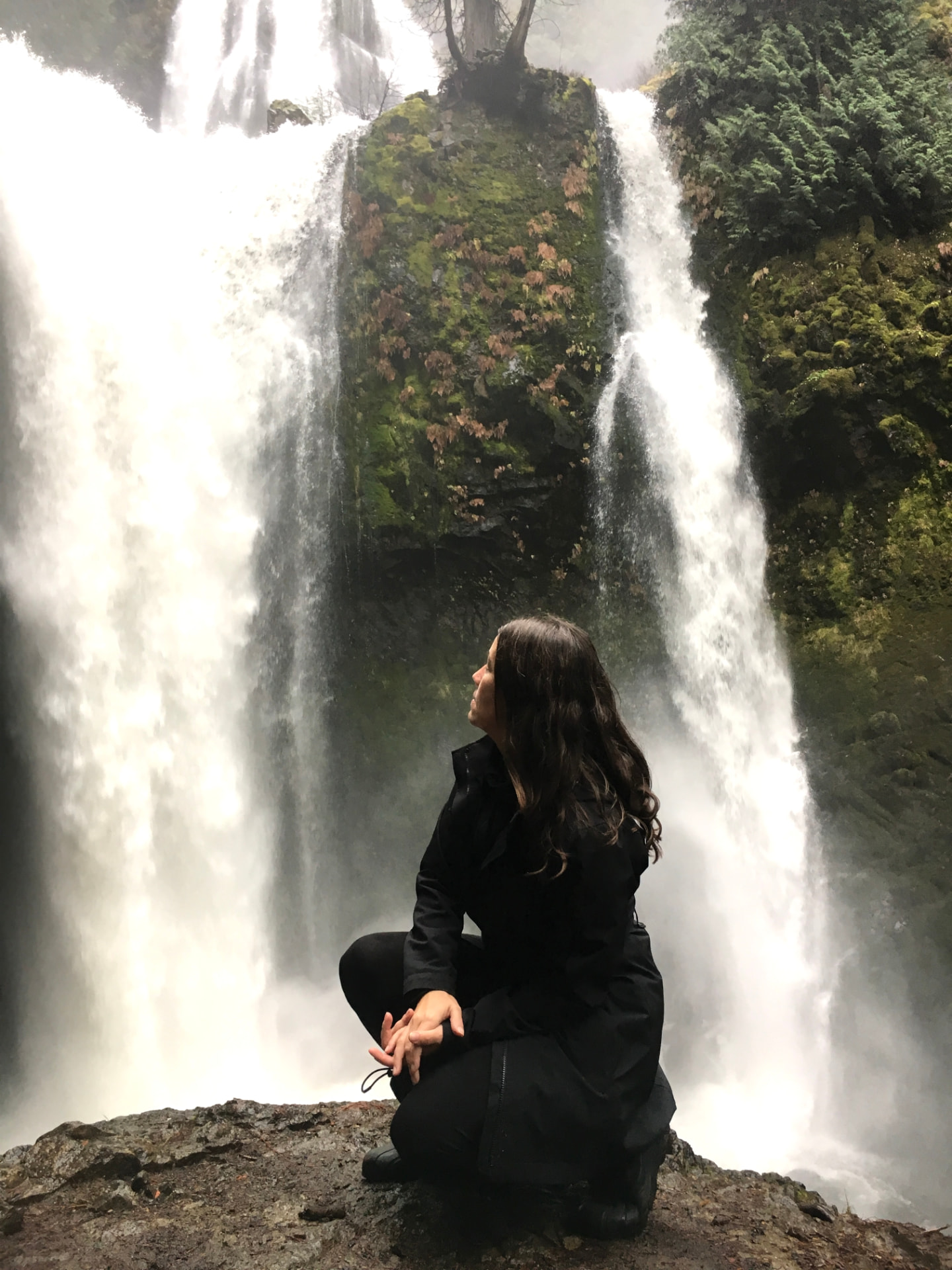 Mary Ostafi seated on a rock before a waterfall